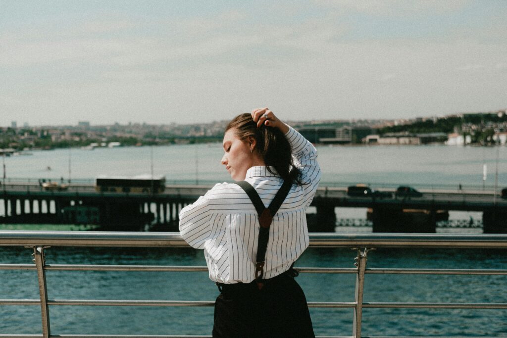 A woman in a striped shirt enjoying a sunny day by the water with an urban bridge view.
